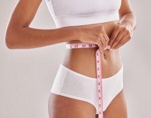 A woman in an exercise outfit measuring her stomach once tirzepatide has left her system after taking it as part of a weight loss plan.
