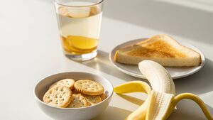 Bland foods including crackers, banana, and toast with water and ginger tea on a bright kitchen table.