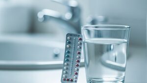 Birth control pill pack and a glass of water on a bathroom counter.